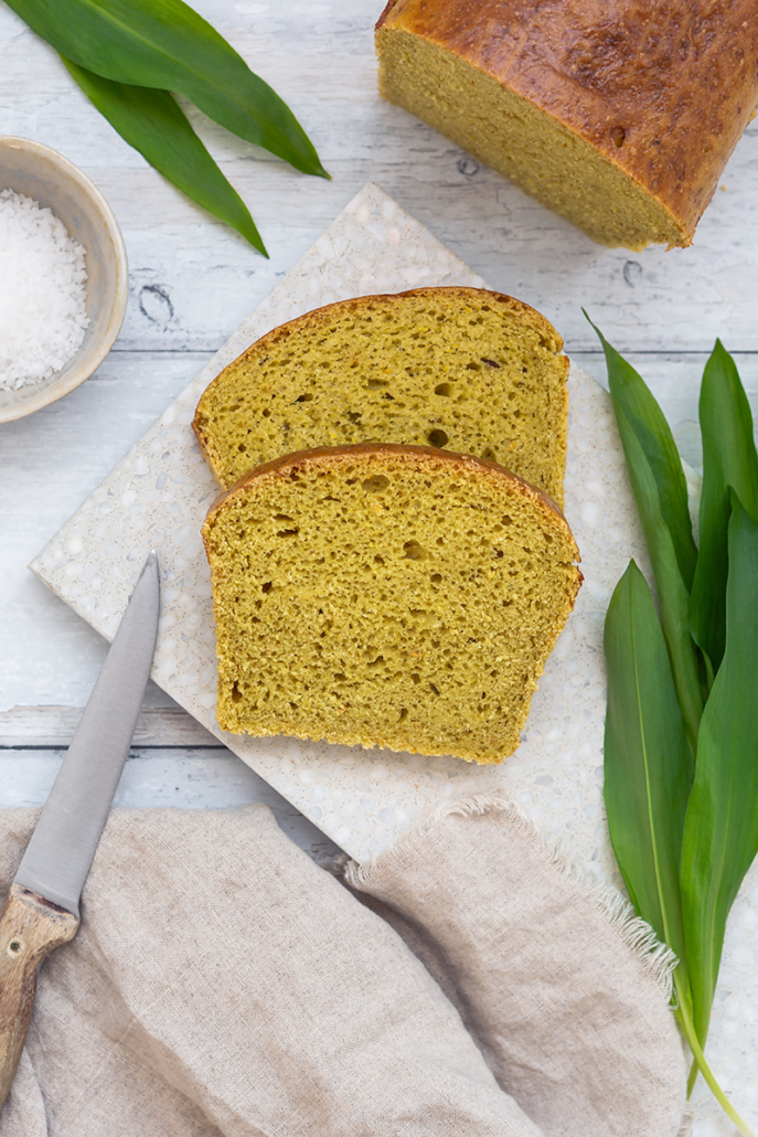 Zwei Scheibe Bärlauch-Brioche liegen auf einem Schneidebrett, daneben steht der angeschnittene Brioche-Laib.